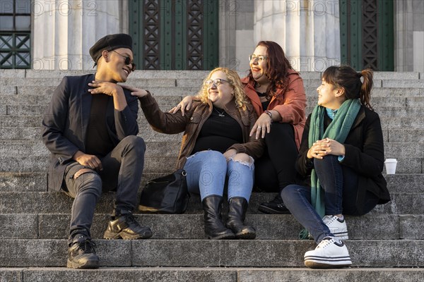 Multi ethnic group of friends sitting on some stairs having a good time chatting and laughing