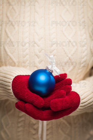 Woman wearing seasonal red mittens holding blue christmas ornament