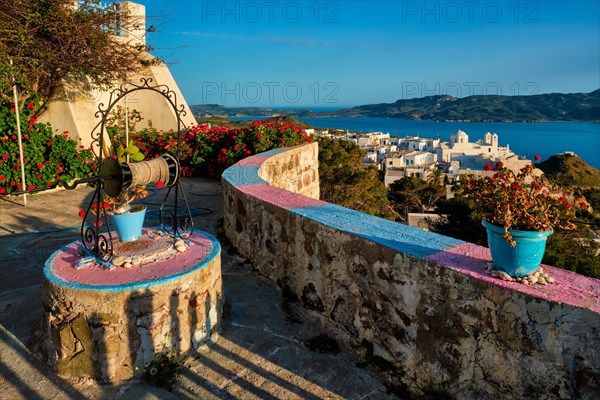 Picturesque scenic view of Greek town Plaka on Milos island over red geranium flowers and Orthodox greek church