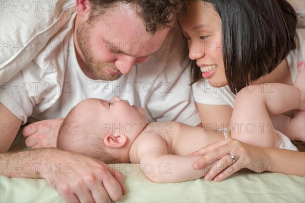 mixed-race chinese and caucasian baby boy laying in bed with his father and mother