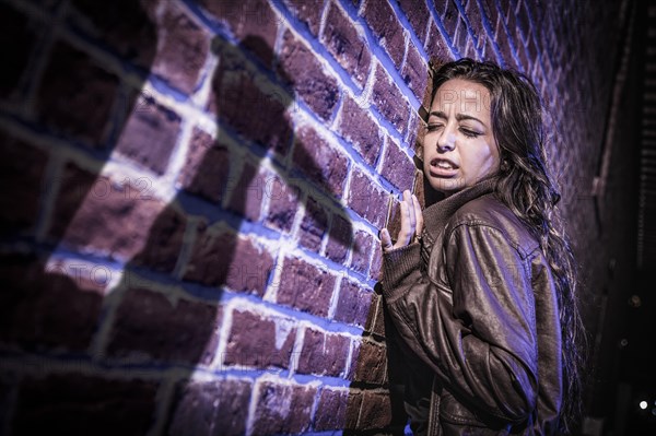 Male shadow figure with knife threatens frightened young woman against brick wall