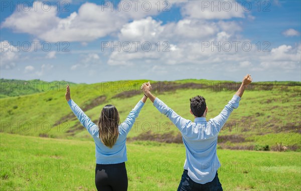 Back view of Happy couple in the field raising hands to the sky