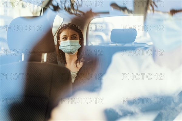 A woman wearing a protective mask sitting on the back seat of a taxi car