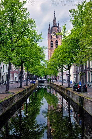 Delt canal with old houses bicycles and cars parked along and Oude Kerk Old church tower. Delft