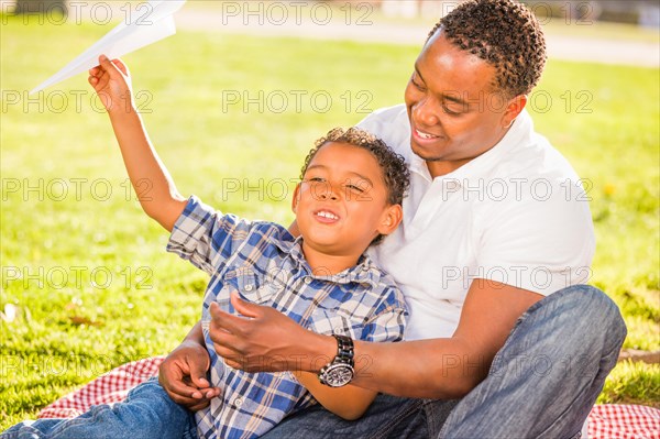 Happy african american father and mixed-race son playing with paper airplanes in the park