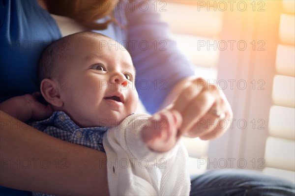 Happy mixed-race couple enjoying their newborn son in the light of the window