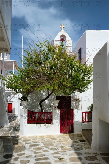 Picturesque scenic narrow Greek streets with traditional whitewashed houses with blue doors windows of Mykonos town and orthodox church in famous tourist attraction Mykonos island