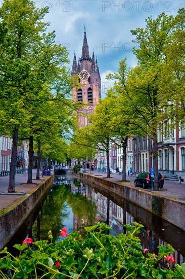 Delt canal with old houses bicycles and cars parked along and Oude Kerk Old church tower. Delft