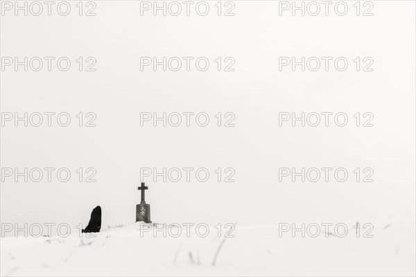 Einsame Frau knieend an Marterl in Winterlandschaft