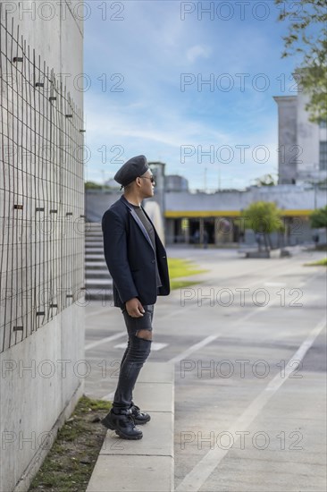 Latin gay male with makeup wearing fashion hat doing catwalk in the street