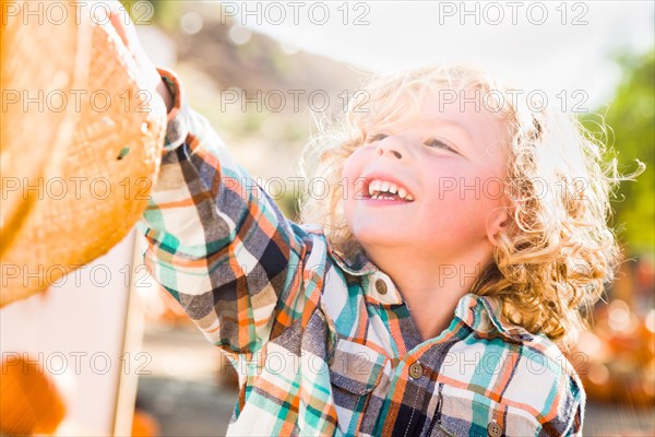 Little boy sitting with A cowboy hat in a rustic ranch setting at the pumpkin patch