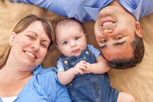 Young mixed-race couple laying with their infant on A blanket