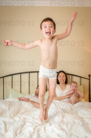 Young mixed-race chinese and caucasian boy jumping in bed with his family