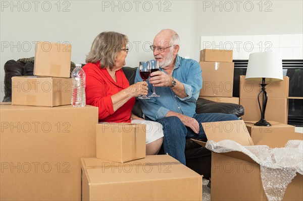 Senior adult couple toasting wine glasses surrounded by moving boxes