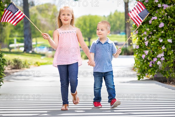 Young sister and brother waving american flags at the park