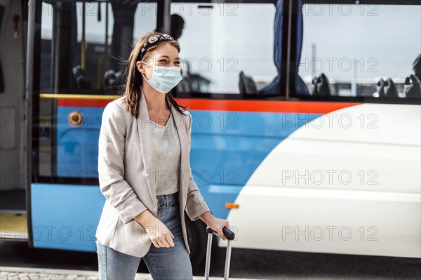 A young woman with mask and luggage has just left the bus after a long trip