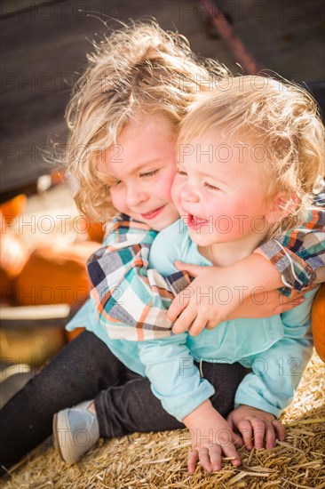 Sweet little boy plays with his baby sister in a rustic ranch setting at the pumpkin patch