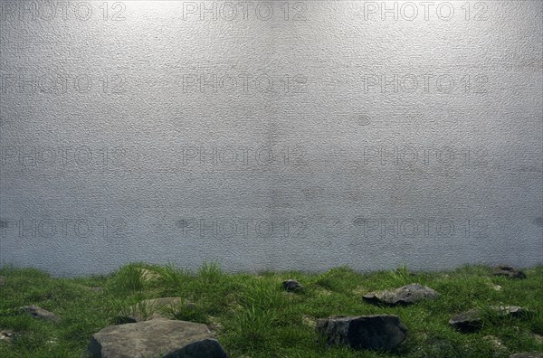Mysterious blank cement wall surrounded by large rocks and grass in field