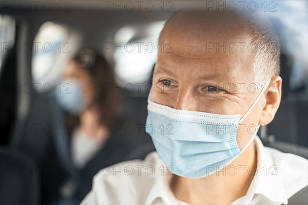 A happy taxi driver wearing a mask and the passenger on the back seat of the car in the background