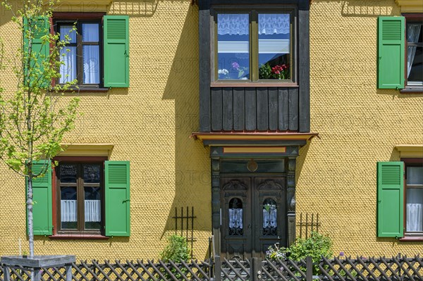 Yellow wooden shingle facade with bay window and green shutters