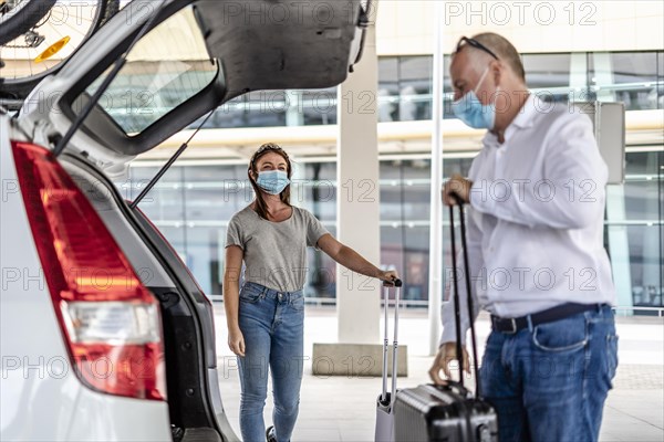 A taxi or Uber driver helping a passenger in a protective mask with her luggage at the airport