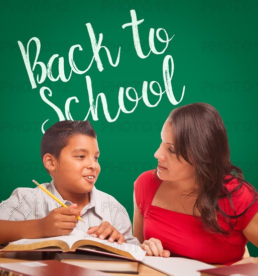 Back to school written on chalk board behind hispanic young boy and famale adult studying