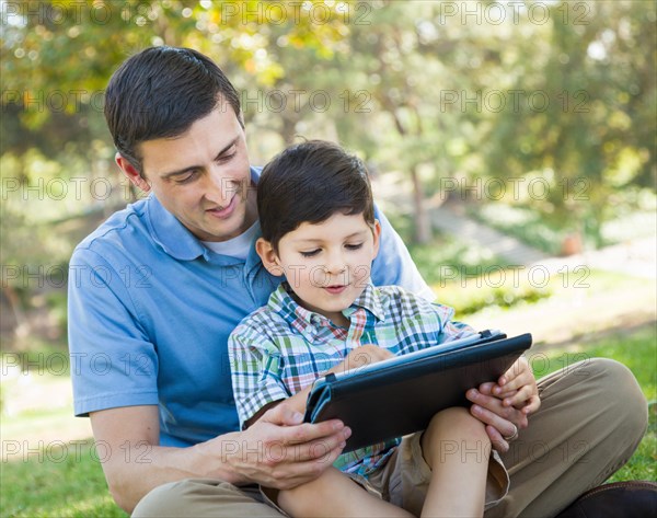 Happy father and son playing on a computer tablet outside