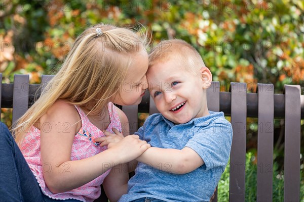 Young sister and brother having fun on the bench at the park