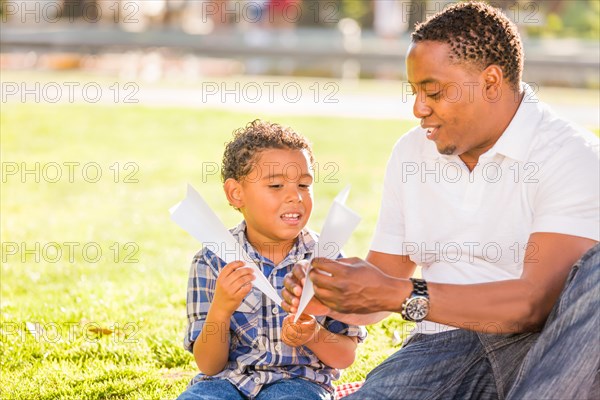 Happy african american father and mixed-race son playing with paper airplanes in the park