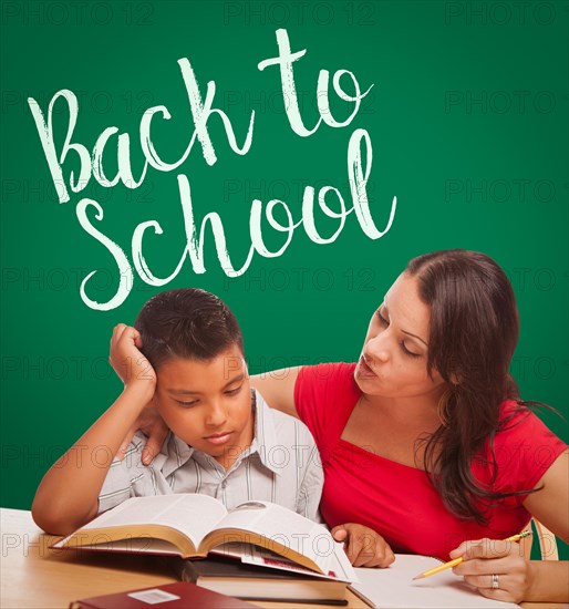 Back to school written on chalk board behind hispanic young boy and famale adult studying