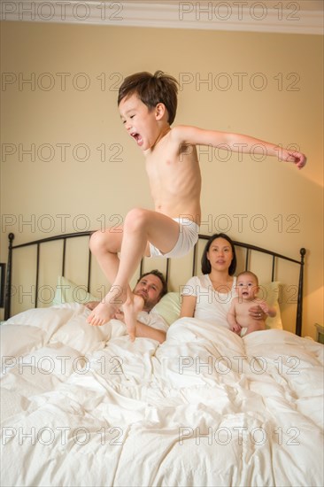 Young mixed-race chinese and caucasian boy jumping in bed with his family