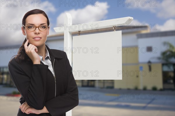 Attractive serious mixed-race woman in front of vacant retail building and blank real estate sign