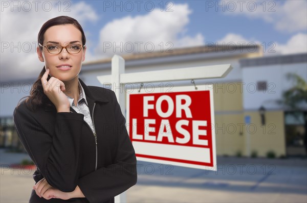 Attractive serious mixed-race woman in front of vacant retail building and for lease real estate sign