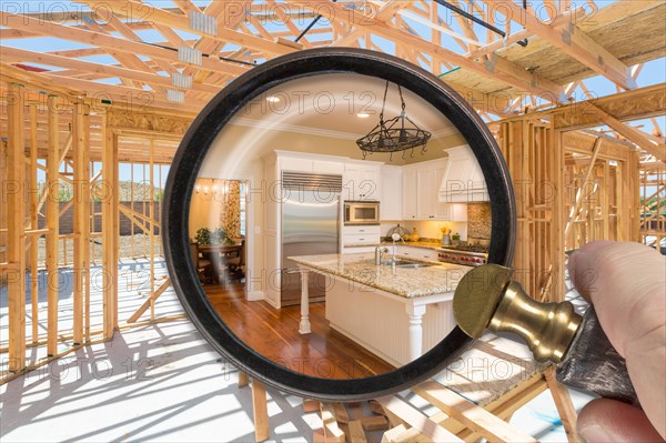 Hand holding magnifying glass revealing finished kitchen build over construction framing