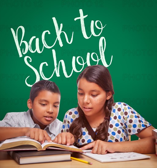 Back to school written on chalk board behind hispanic boy and girl having fun studying together