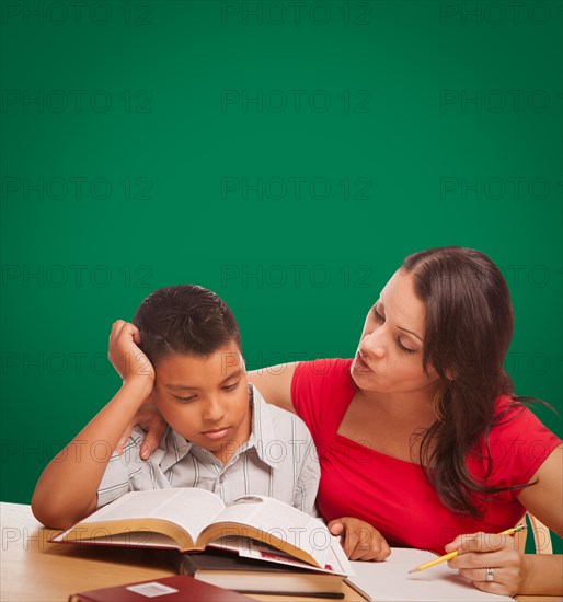 Blank chalk board behind hispanic young boy and famale adult studying