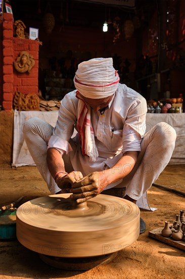 Indian potter at work: throwing the potter's wheel and shaping ceramic vessel and clay ware: pot