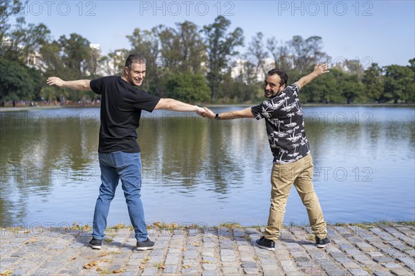 Homosexual mature white male couple holding hands smiling at a lake