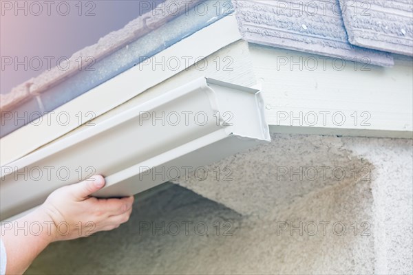 Worker attaching aluminum rain gutter to fascia of house