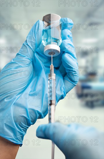 Doctor or nurse wearing surgical gloves holding vaccine vial and medical syringe within hospital