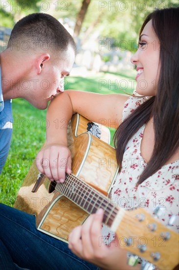 Young adult girl playing guitar with boyfriend in the park