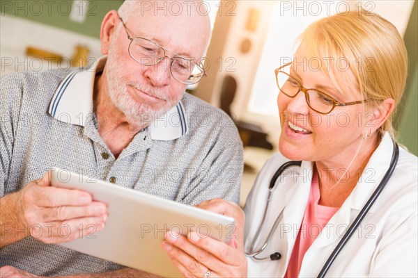 Female doctor or nurse showing senior man touch pad computer at home