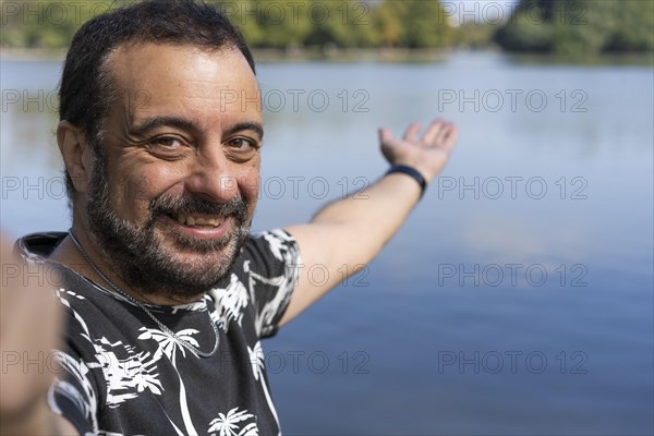 Active handsome mature Caucasian man taking selfie showing around at a lake. Outdoor adventure concept