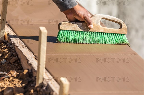 Construction worker using brush on wet cement forming coping around new pool