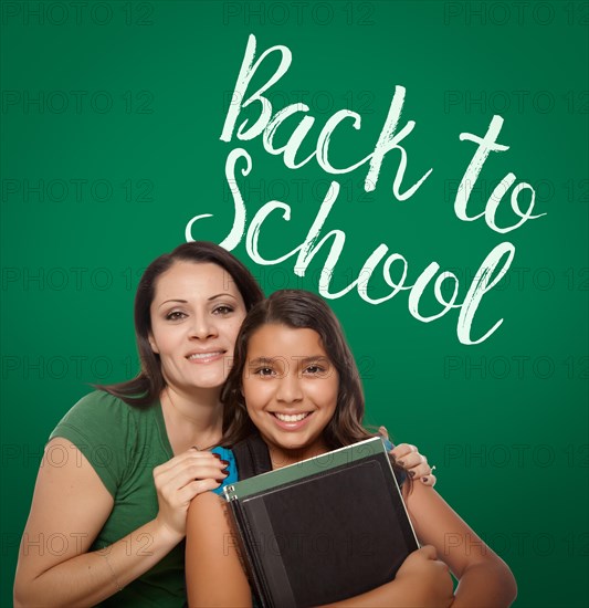 Back to school written on chalk board behind proud hispanic mother and daughter student
