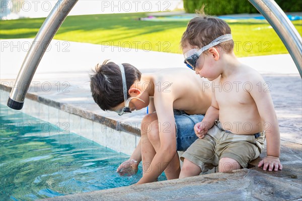 Young mixed-race chinese and caucasian brothers wearing swimming goggles playing at the pool