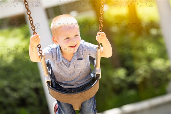 Happy young boy having fun on the swings at the playground