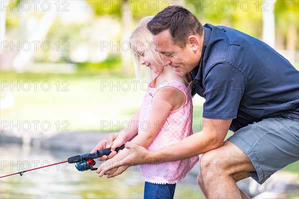 Young caucasian father and daughter having fun fishing at the lake