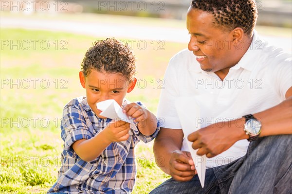 Happy african american father and mixed-race son playing with paper airplanes in the park