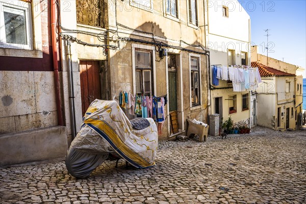 Steep street of Sesimbra downtown with covered motorbike